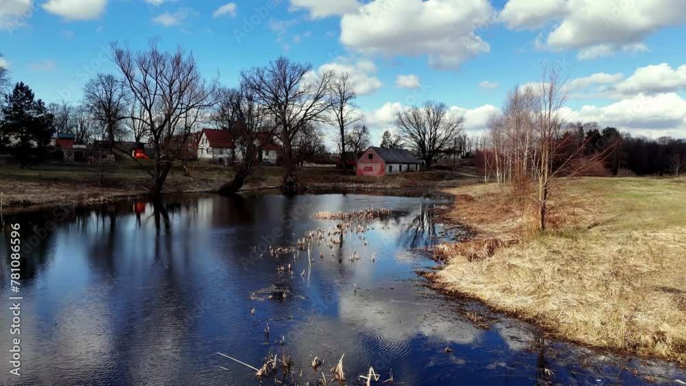 Calm lake with a house in the background, pond with clear water reflecting a bright blue sky with white clouds Calm lake with a house in the background, pond with clear water reflecting a bright blue sky with white clouds