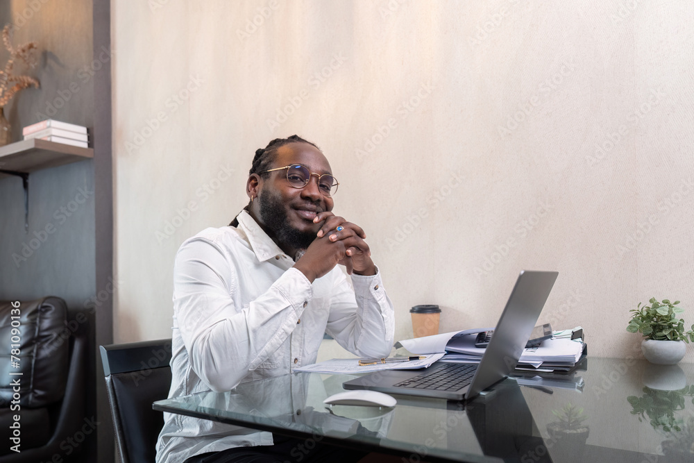 Smiling African American man sit at desk in home working on laptop, happy African American male look at camera posing, busy using modern computer gadget at home