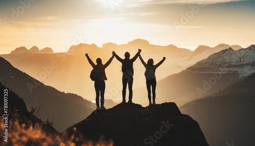 celebrate victory and success over sunset background together overcoming obstacles as a group of three people raising hands up on the top of a mountain #781097325