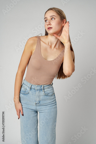 Young woman puts a hand to the ear to hear better on gray background