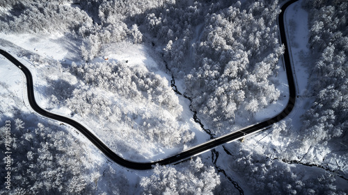 An aerial perspective showcases the stark contrast between the winding road, cutting a dark path through a dense forest blanketed with snow. KRASNAYA POLYANA, SOCHI, RUSSIA – winter JANUARY: «Laura».