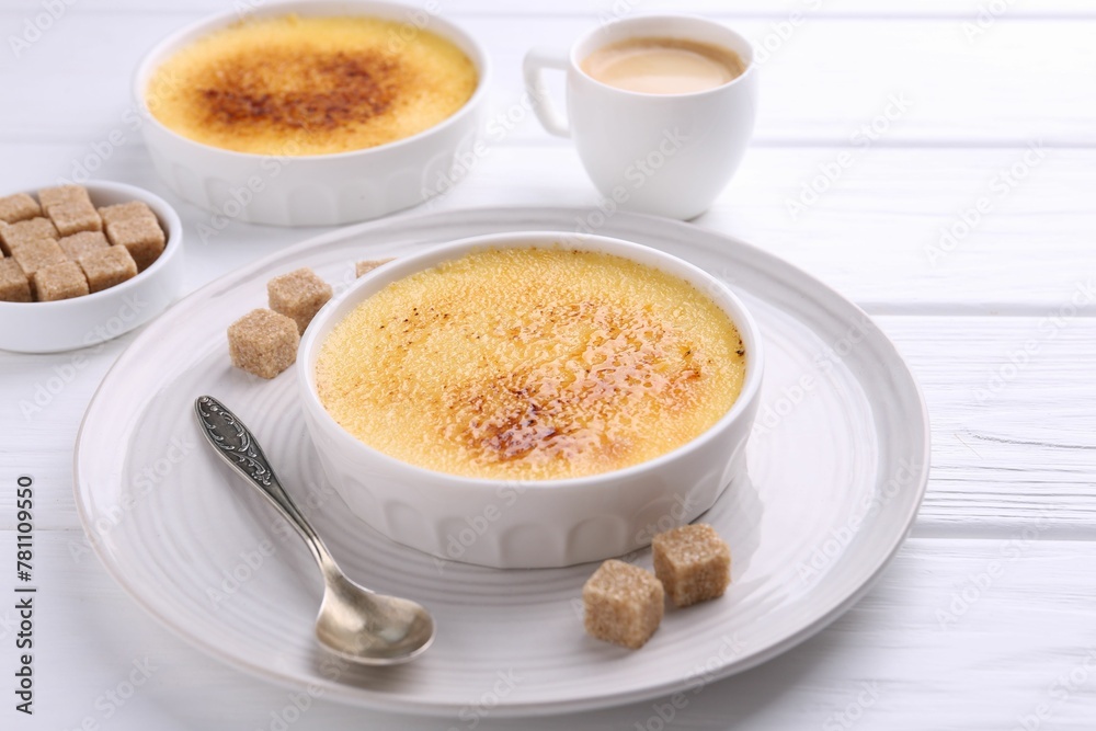 Delicious creme brulee in bowls, vanilla pods, sugar cubes and coffee on white wooden table Delicious creme brulee in bowls, vanilla pods, sugar cubes and coffee on white wooden table