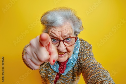  funny angry granny threatens with her finger. elderly woman on yellow background. grandma looks at the camera