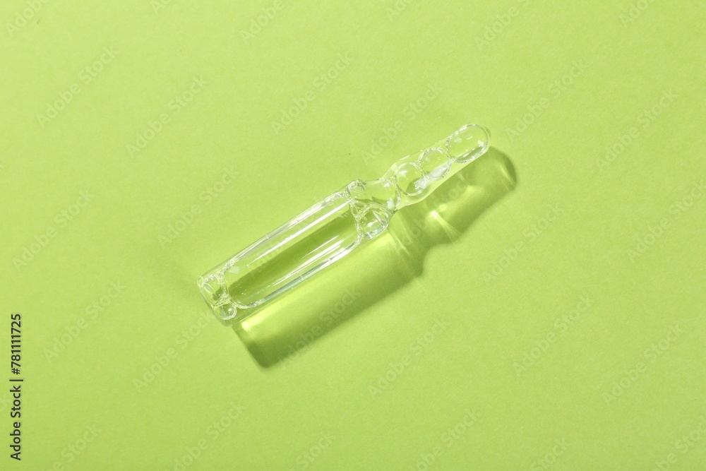 Glass ampoule with liquid on light green background, top view Glass ampoule with liquid on light green background, top view