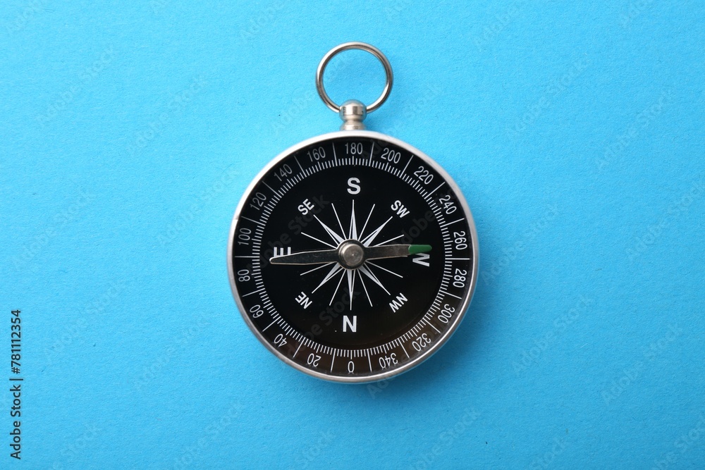 One compass on light blue background, top view. Tourist equipment