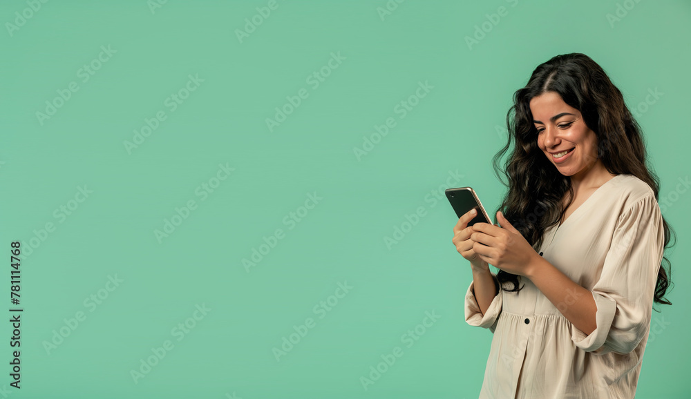 Woman on mint background looking at phone and smiling
