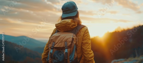 Back view of young woman in cap with backpack, sunset mountains   outdoor travel concept photo
