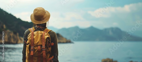 Young woman in hat with backpack, back view, summer travel concept, sea and mountain background