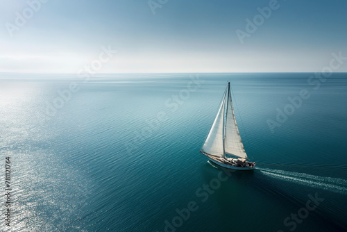 A sailboat glides over a calm blue ocean under a clear sky, leaving a gentle wake trailing behind.
