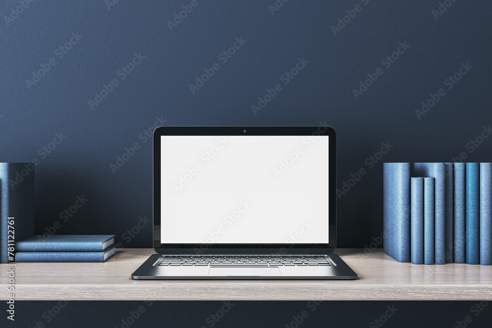 Fototapeta premium Close up of creative wooden designer desk with books and empty white mock up laptop screen on blue concrete wall. 3D Rendering.