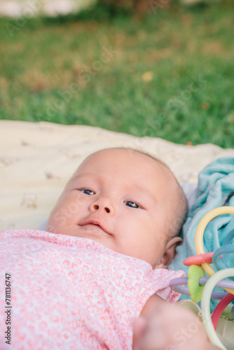Infant Baby Girl is laying on her back in a pink bodysuit with a development toy for teething.