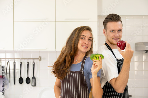 Portrait of smiling loving couple family standing at the kitchen. Male holding apple while female holding broccoli and looking at camera