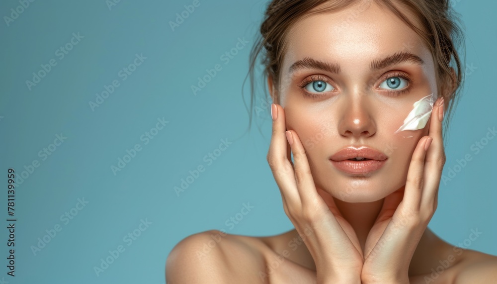 Young woman with a fresh, natural look applying moisturizing cream on her face against a serene blue background. Beauty concept Young woman with a fresh, natural look applying moisturizing cream on her face against a serene blue background. Beauty concept