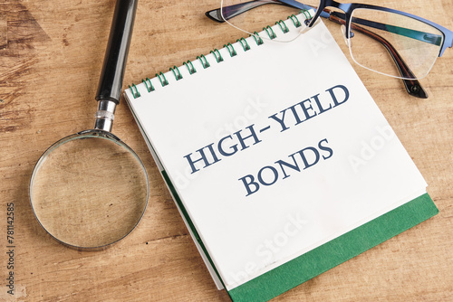 Inscription High-Yield Bonds on a notebook with a magnifying glass and glasses on a vintage background photo