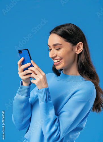 Woman on a blue background looks at the phone and smiles
