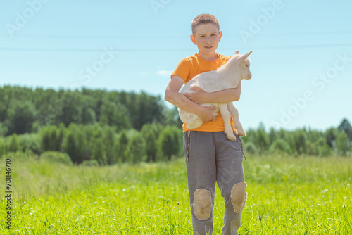 A young boy in an orange shirt standing in a field holding a white goat