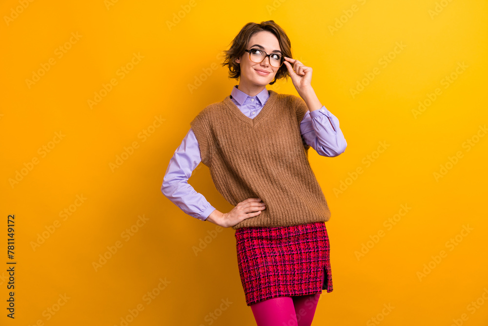 Fototapeta premium Photo of adorable smart girl dressed knitwear waistcoat touch glasses look at discount empty space isolated on yellow color background