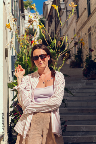 A young girl in sunglasses travels through Europe and poses against the background of a long staircase and potted plants growing on the staircase street
