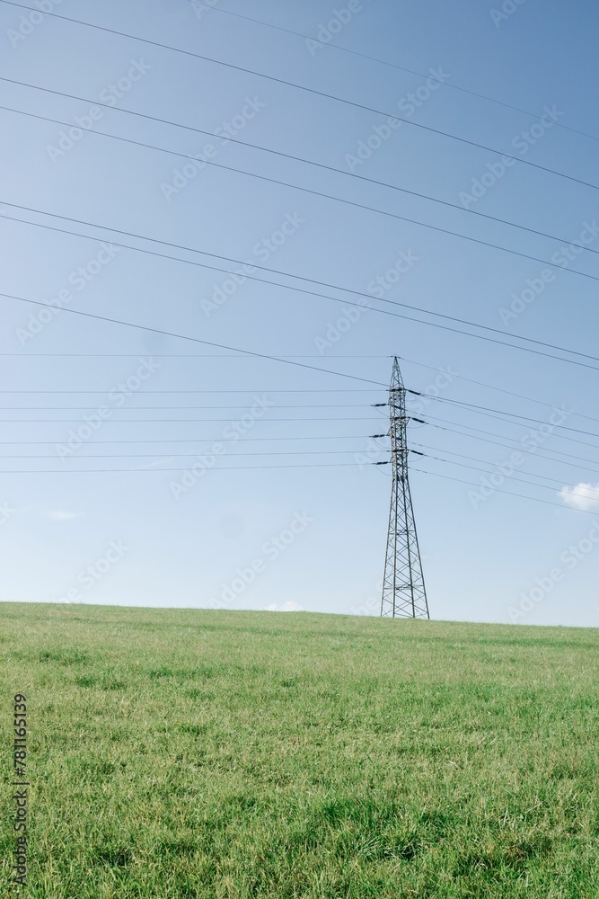hi-voltage electric poles with cable lines at green field under clear blue sunny sky in landscape