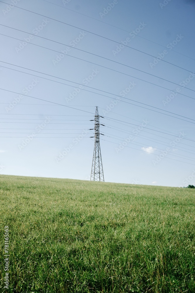 Vertical shot of a high-voltage steel pylon tower with electric lines on a rural green field