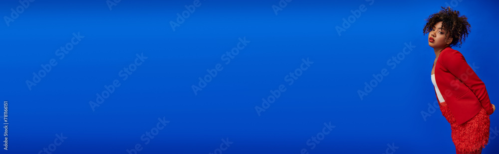 chic african american woman in red blazer with curly hair looking at camera, blue backdrop, banner chic african american woman in red blazer with curly hair looking at camera, blue backdrop, banner