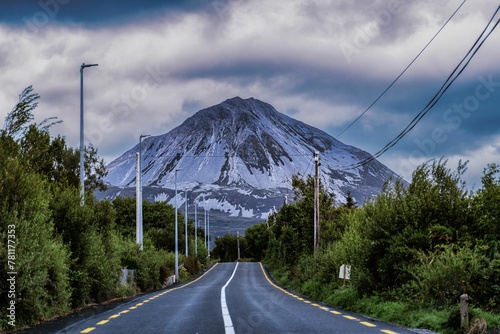 Road surrounded by trees leads to Errigal mountain on a cloudy day