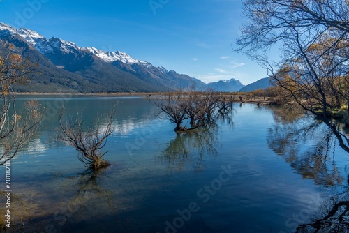 Fototapeta Naklejka Na Ścianę i Meble -  Mesmerizing shot of lake and dry bushes, mountains in the background with their reflection in water