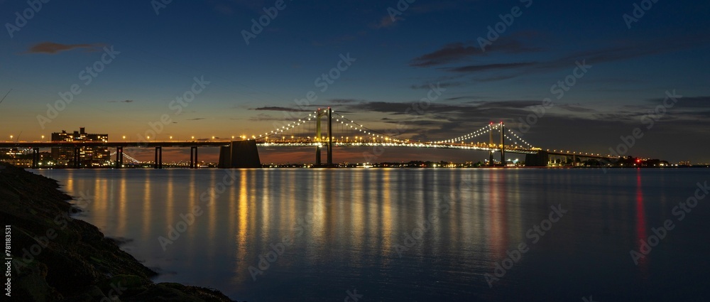 Beautiful shot of a sea with the background of an illuminated bridge and the sunset sky