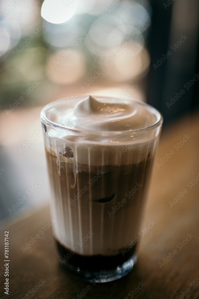 Vertical shot of a foamy coffee put on the wooden table on the blurred background Vertical shot of a foamy coffee put on the wooden table on the blurred background