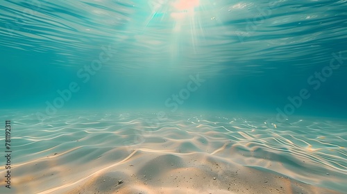 Blue tropical ocean above, seabed sand below, empty underwater background with the summer sun shining brightly, creating ripples in the calm sea water.