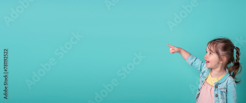 A little girl on a turquoise background points her finger to the side. Free space for text. 