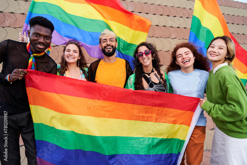 Cheerful portrait of group of diverse LGBTQI people holding rainbow flags, looking at camera happily, celebrating the pride day together supporting the gay community. Copy space.
