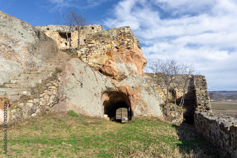 Inside of Medieval fortress on a rock. Stone walls and staircase.  Entrance to the courtyard through a rock tunnel. Bright blue sky with clouds.  Kveshi fortress. Georgia