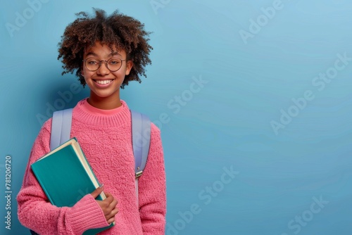 A young girl wearing a pink sweater and glasses is holding a book. She is smiling and she is happy photo