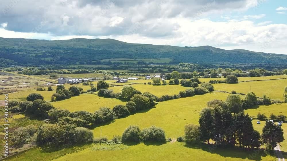 Aerial of. a green field with green hills and forests in the background under the cloudy sky