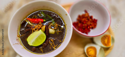 Rawon or Indonesian black beef soup, black color are from indonesian nut called kluwek. Served with lime, chili paste, salted egg, and tempe cracker. Perfect for recipe, article, or any cooking conten
