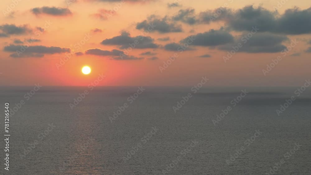 Aerial view of an orange sunset over a calm ocean on a cloudy day Aerial view of an orange sunset over a calm ocean on a cloudy day