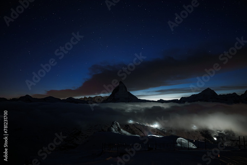 Breathtaking night scene at Zermatt ski resort, Matterhorn mountain silhouetted against starry sky. Tranquil with hint of human activity, serene natural beauty.