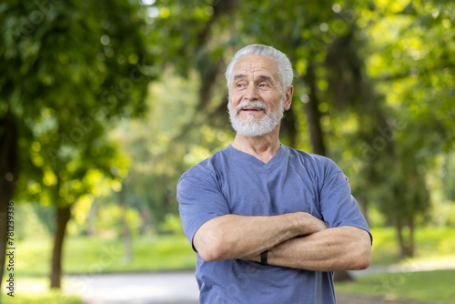 A close-up photo of an older gray-haired man standing in casual clothes in nature, crossing his arms on the ground and looking to the side with a smile. © Liubomir