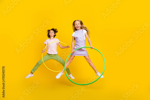Full length photo of cute funky friends wear casual outfits jumping high playing hoola hoops isolated yellow color background photo