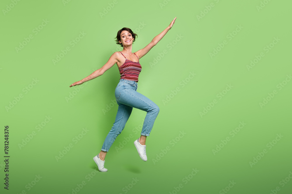 Full length photo of carefree positive cute girl wear stylish outfit flying air going empty space isolated on green color background Full length photo of carefree positive cute girl wear stylish outfit flying air going empty space isolated on green color background