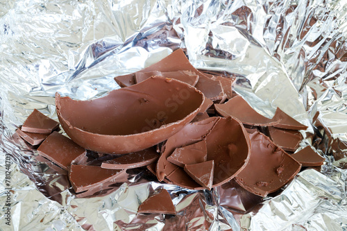 Un uovo di Pasqua di cioccolato al latte rotto in pezzi su fondo argentato. Pasqua e periodo festivo.