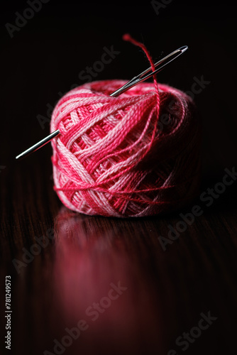 A needle with a large eye is stuck into a skein of colorful threads. Selective focus.