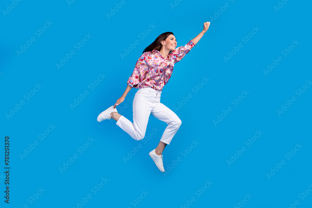 Full length photo of funky cheerful lady dressed print shirt jumping high running empty space isolated blue color background