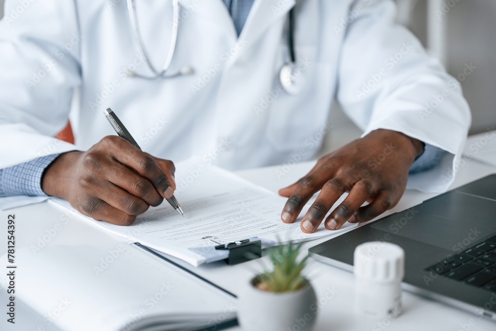 Filling in the document, writing by using pen. Black man as doctor in the clinic office Filling in the document, writing by using pen. Black man as doctor in the clinic office
