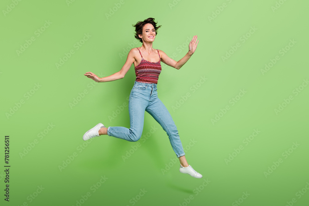 Full length photo of positive cute girl wear stylish clothes flying air good mood isolated on green color background