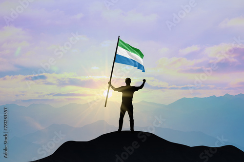 Sierra Leone flag being waved by a man celebrating success at the top of a mountain against sunset or sunrise. Sierra Leone flag for Independence Day. photo