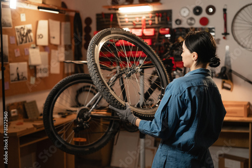 Caucasian young female worker holding and repairing bicycle wheel in bicycle workshop or authentic garage.