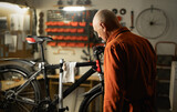 Mature male repairman repairing bicycle in garage or workshop, looking on wheel. Bike service, repair and upgrade concept