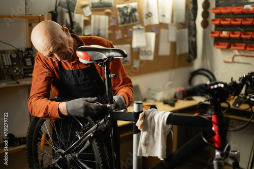Old male mechanic working in bicycle repair shop, mechanic repairing bike. photo